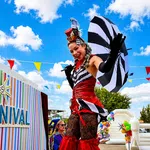 Performers in colorful carnival costumes entertain at LASPCA's outdoor community carnival event under a bright blue sky.