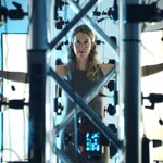 Woman standing inside a 3D scanning rig with arms outstretched surrounded by cameras and lighting panels.