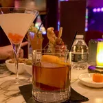 Cocktails served on a marble table with dim lighting and a water bottle in a cozy bar setting.