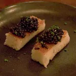 Two rectangular pieces of toasted bread topped with black caviar and garnished with chopped chives on a dark plate
