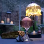 Elegant cocktail glass with a pink spherical garnish on a table beside a decorative lamp and fortune cookies.