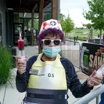 Person in nurse costume wearing sunglasses and mask holding two large syringes outside a building.