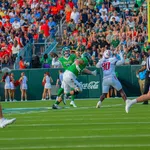 Tulane quarterback prepares to throw under pressure from defenders with crowd and cheerleaders in background