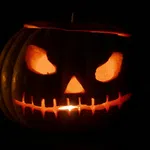 Glowing Halloween jack-o'-lantern with menacing eyes and stitched mouth carved in pumpkin in darkness