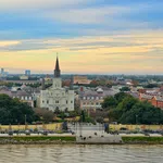 Stunning view of St. Louis Cathedral and Jackson Square with the Mississippi River in the foreground at sunset.