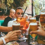 Group of friends clinking glasses with beer and cocktails at an outdoor social gathering.
