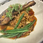 Grilled pork chop with green beans, rice, and sauce garnished with fresh herbs in a white bowl.