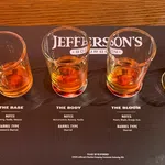 Four whiskey tasting glasses with varying bourbon samples on a Jefferson's Bourbon tasting mat showing flavor notes and barrel types.