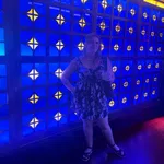 Woman in a floral dress standing in front of a vibrant blue and yellow patterned illuminated wall.
