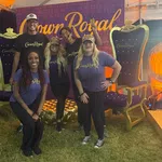 Five people wearing Crown Royal shirts pose in front of a Crown Royal backdrop between two large decorative royal chairs.