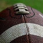 Close-up of a textured brown and white American football showing laces and pebbled surface detail.