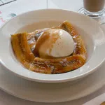 Grilled plantains topped with vanilla ice cream and caramel sauce in a white bowl on a white table.