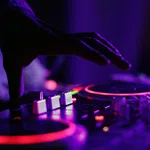 Close-up of a DJ's hand adjusting controls on a colorful illuminated mixer in a dark room.