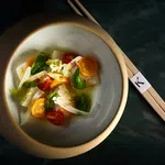 Elegant bowl of fresh vegetable salad with cherry tomatoes, greens, and chopsticks on dark surface.