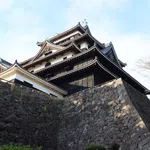 Traditional Japanese castle with multi-tiered roofs atop large stone walls under a clear sky.