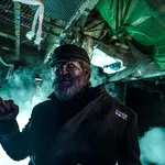 Dark haunted captain with a hook hand and eerie blue lighting in a spooky, fog-filled ship interior.