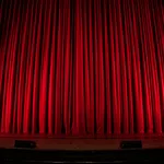 Closed red theater curtains illuminated on a stage ready for a performance.
