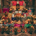 Traditional Mexican Day of the Dead altar decorated with marigolds, papel picado, photos, skeletons, and food offerings.