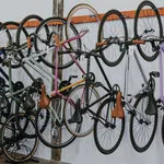 Multiple bicycles with leather seats hanging on wall racks and others parked on the floor in a bike shop.