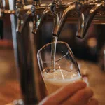 Beer being poured from a tap into a tilted glass at a bar with blurred background.