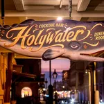 Hanging whale-shaped wooden sign for Holy Water oyster house, cocktail bar, and dining room at dusk.