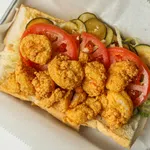 Fried shrimp po'boy sandwich with sliced tomatoes, pickles, and lettuce on a sub roll.