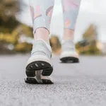 Close-up of a person walking on pavement wearing gray running shoes and floral leggings outdoors.
