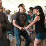 Couples dancing energetically in a lively indoor social dance event under a white tent