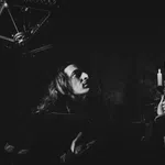 Black and white photo of a person holding a candelabra with burning candles in a dark, gothic setting.