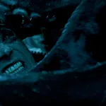 Close-up of a man's tense face underwater surrounded by tentacles in dark blue lighting.