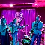 Live band performing with guitar, saxophone, vocals, and keyboard on stage at Chickie Wah Wah venue.