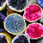 Close-up of colorful geode crystals in shades of purple, blue, pink, and black with rough outer shells.