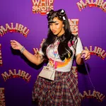 Woman with styled hair and plaid skirt poses in front of purple backdrop with Malibu and Whip Shots logos.
