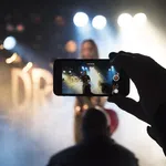 Person recording a live music performance on smartphone with stage lights and smoke effects in background