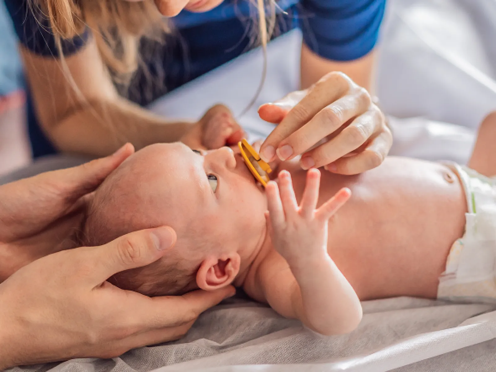 Mother placing a pacifier in a newborn baby's mouth while father gently supports the baby's head.