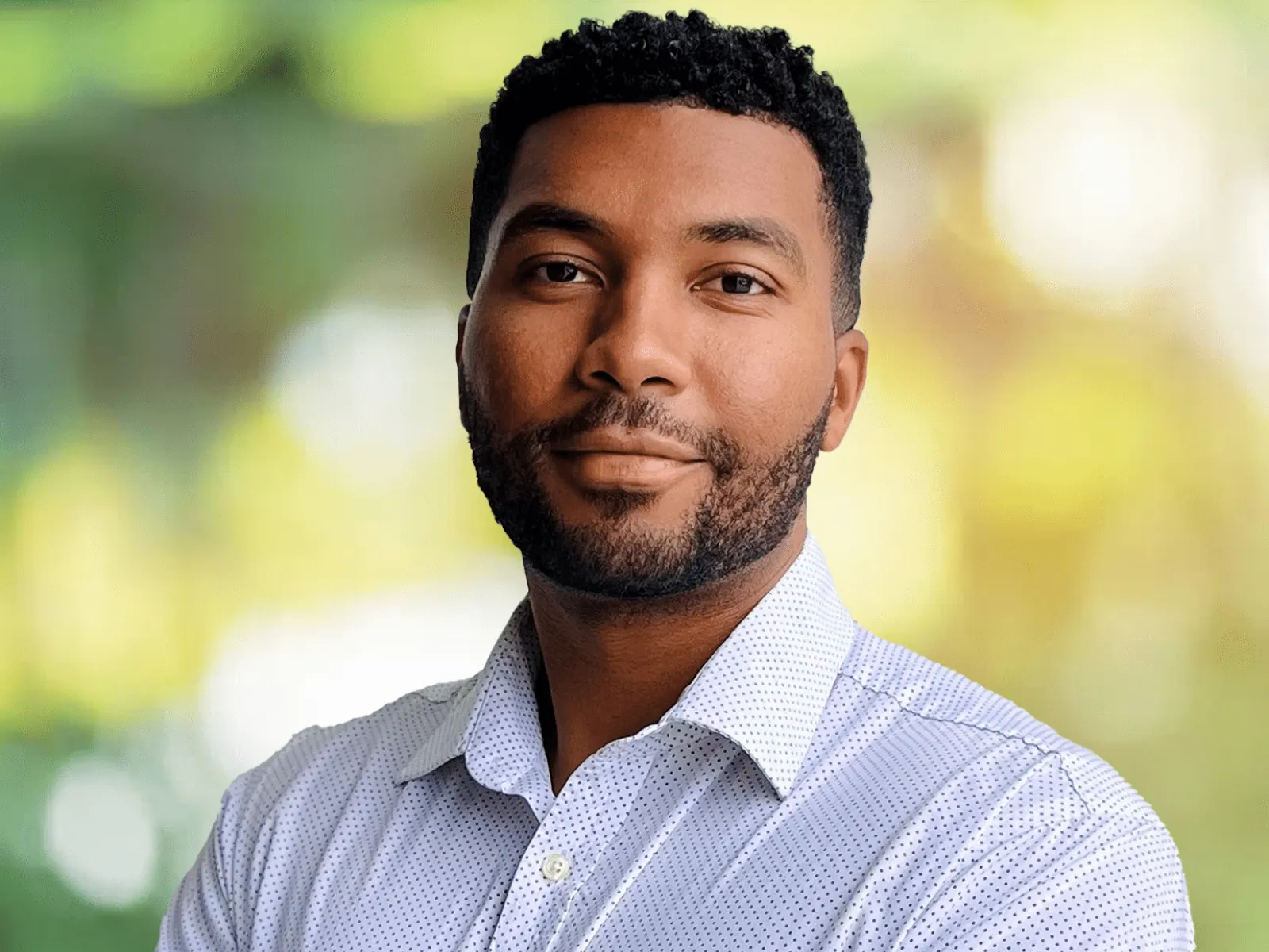 Portrait of confident young man with beard in white shirt against blurred green background