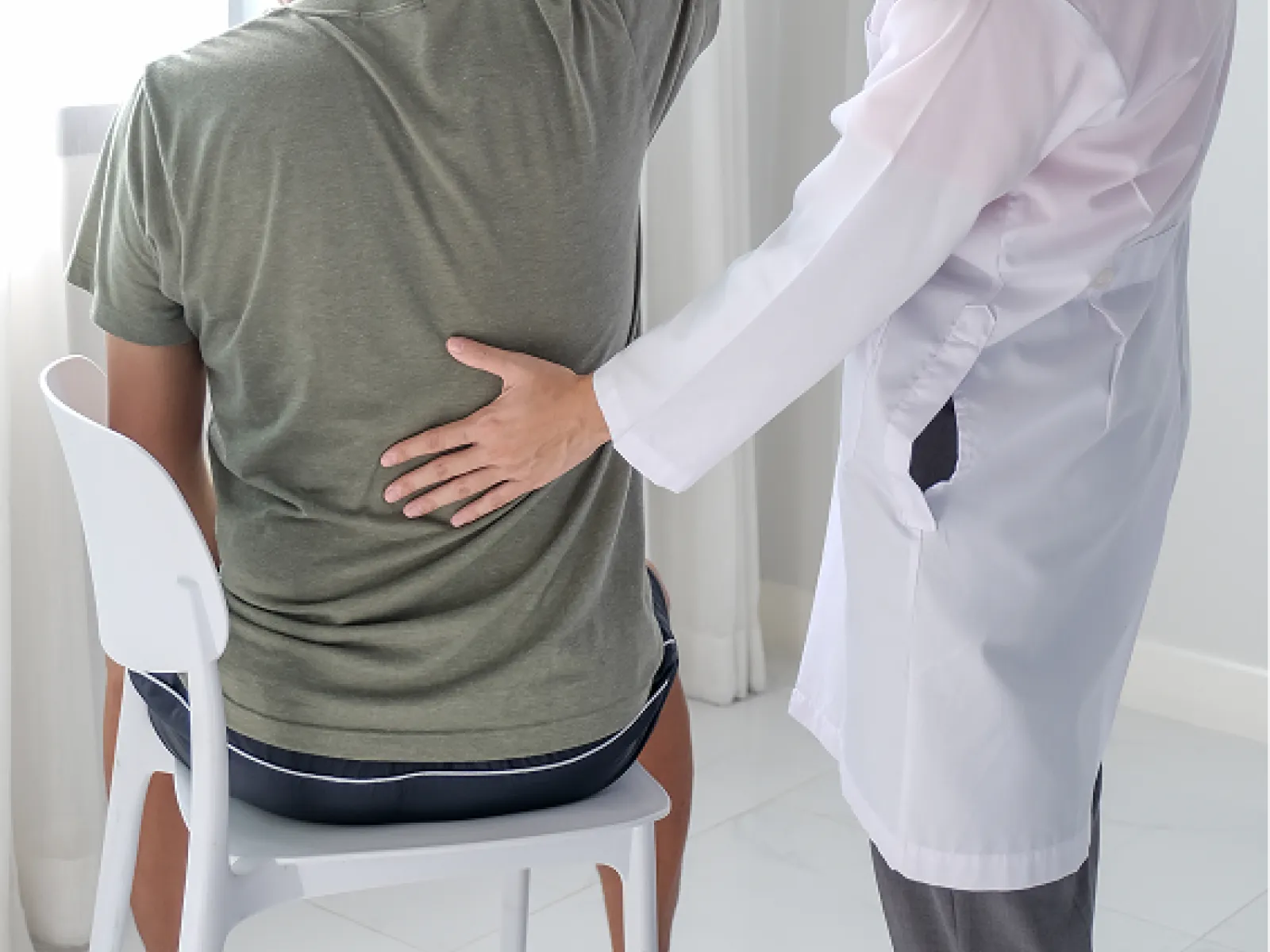 Physical therapist assisting seated man with arm stretch in bright room by window.