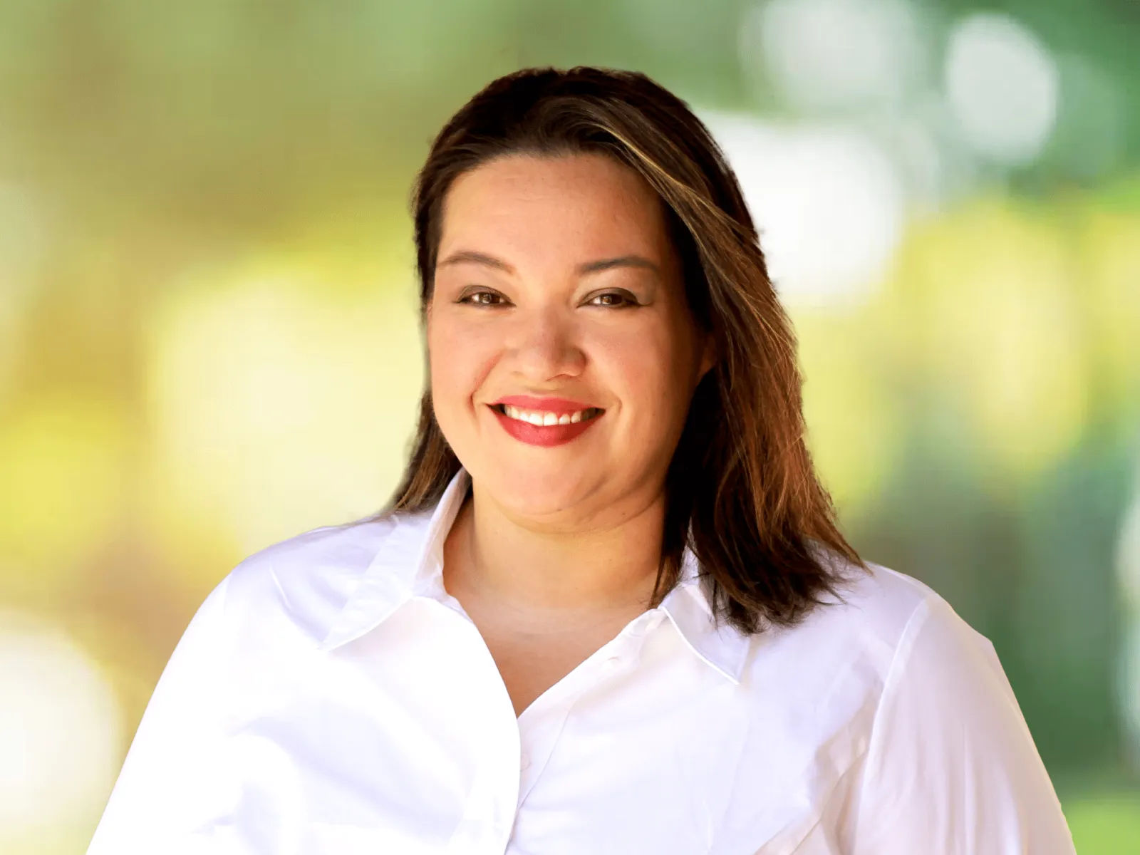 Smiling woman in a white shirt standing outdoors with a bright green blurred background