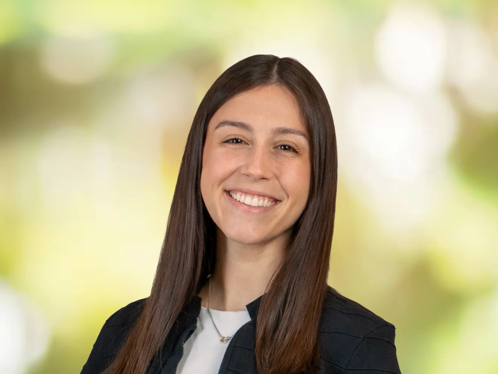 Smiling young woman with straight brown hair wearing a black jacket against a blurred bright green background