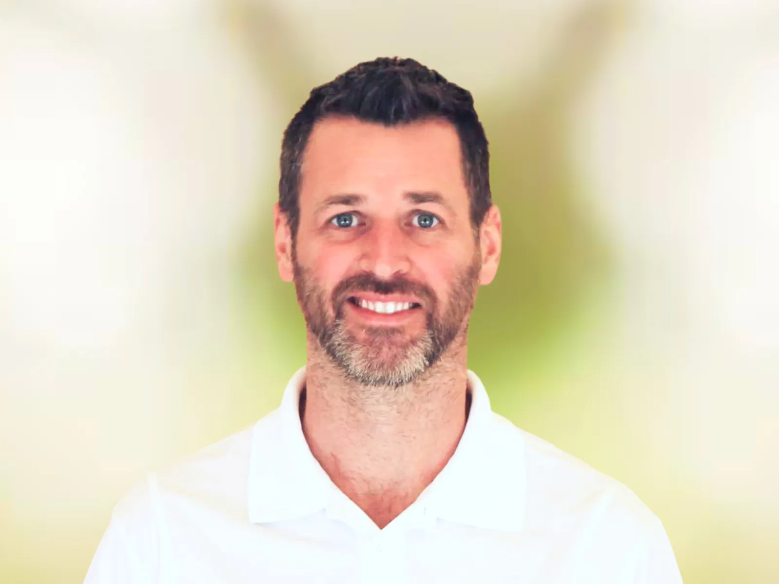 Smiling man with short dark hair and beard wearing a white polo shirt with 100% Chiropractic logo