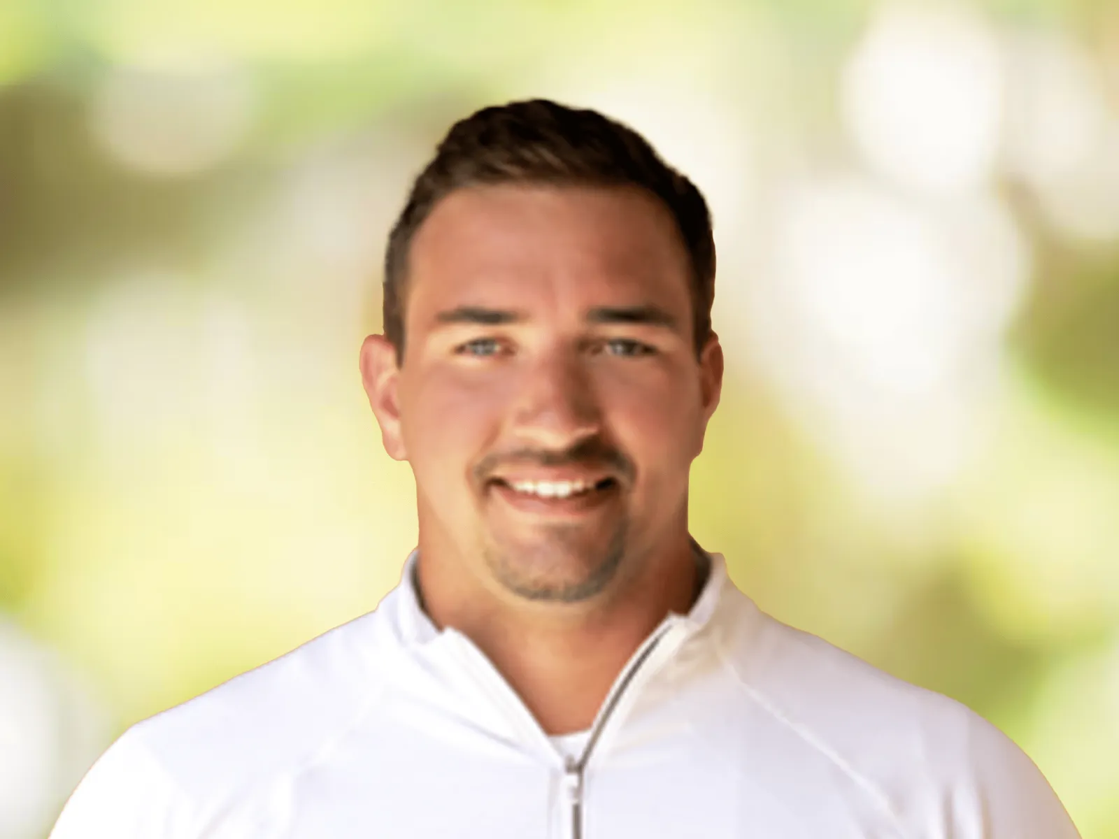 Smiling man wearing a white zip-up jacket with a blurred natural background behind him