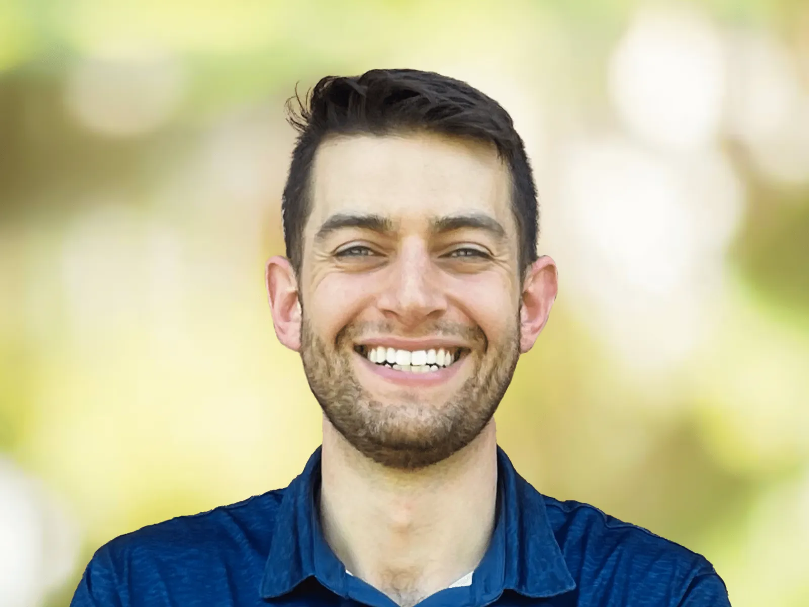 Smiling young man with short dark hair and beard wearing a navy blue polo shirt outdoors