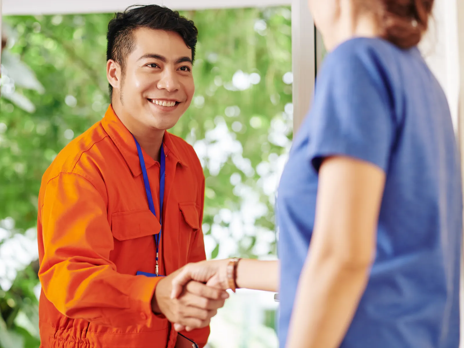 A smiling service technician in orange uniform shakes hands with a customer indoors.