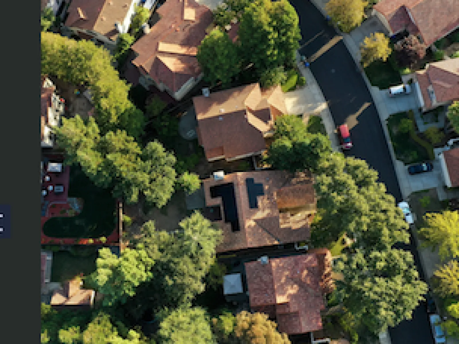 Aerial view of suburban neighborhood with trees, houses, and cars along curved streets on a sunny day