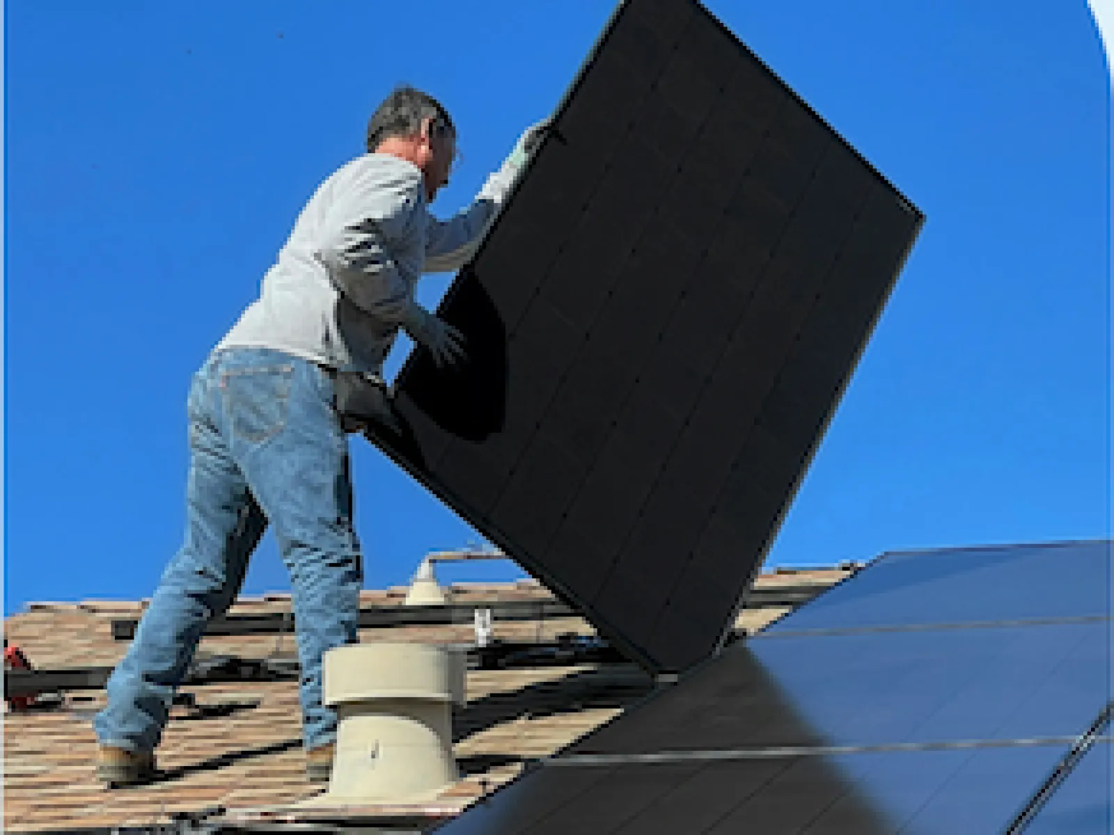 Technician installing a solar panel on a rooftop under clear blue sky for solar energy setup