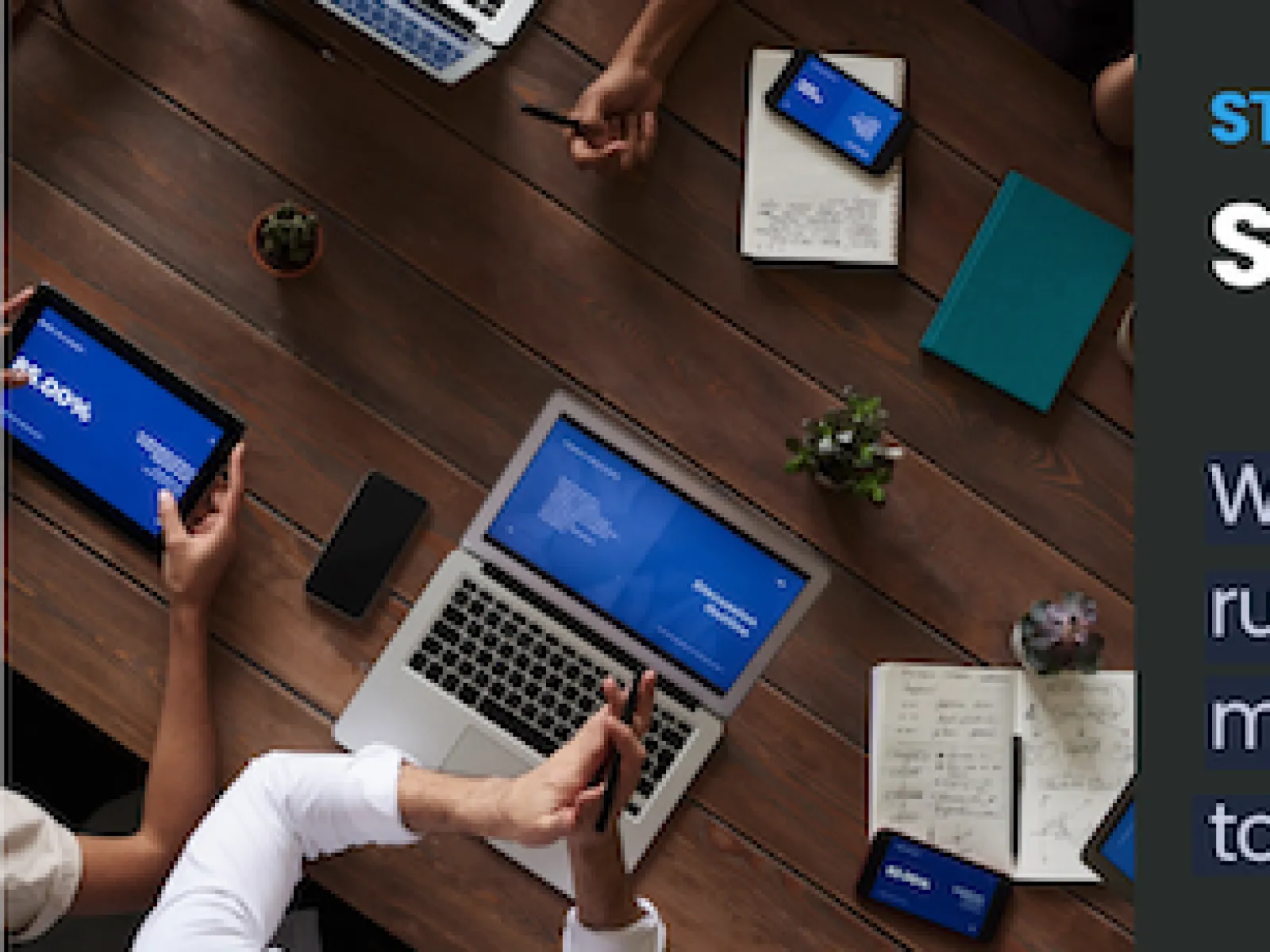 Top view of a collaborative meeting with laptops, tablets, smartphones, notebooks, and plants on a wooden table