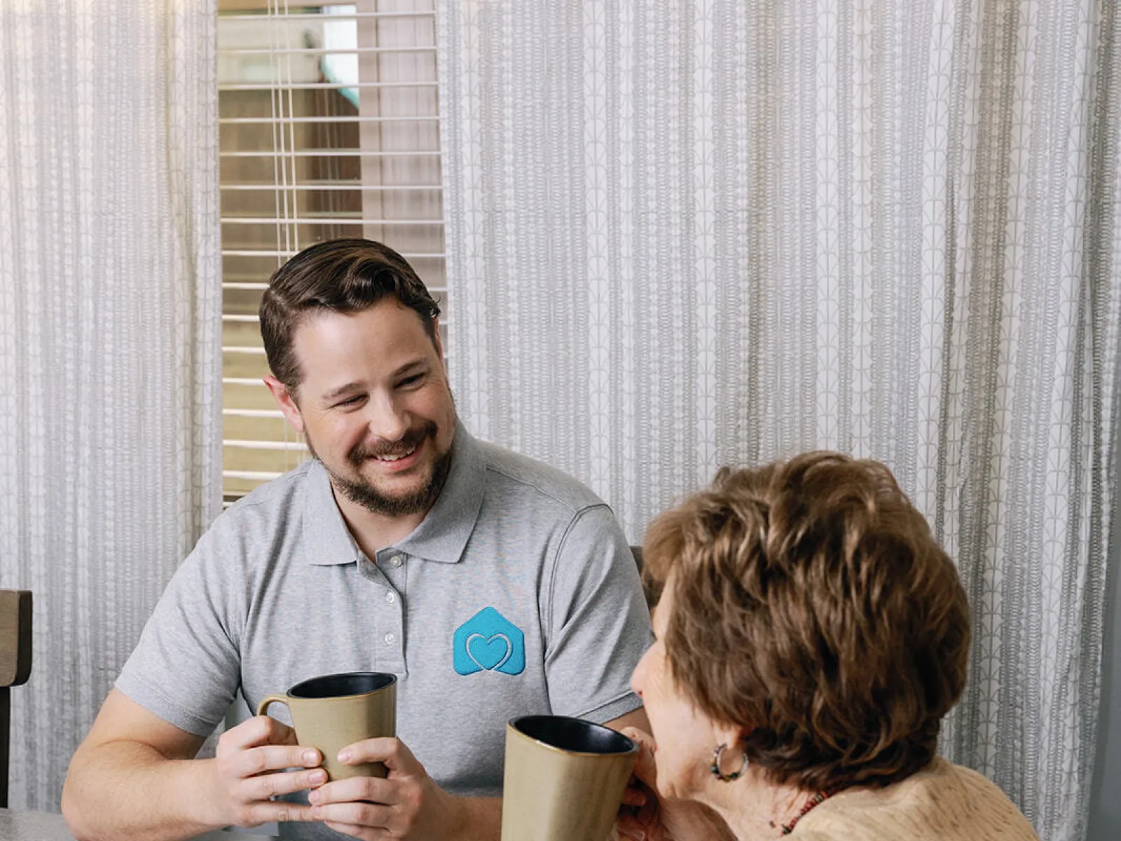 a caregiver and woman sitting at a table with coffee cups