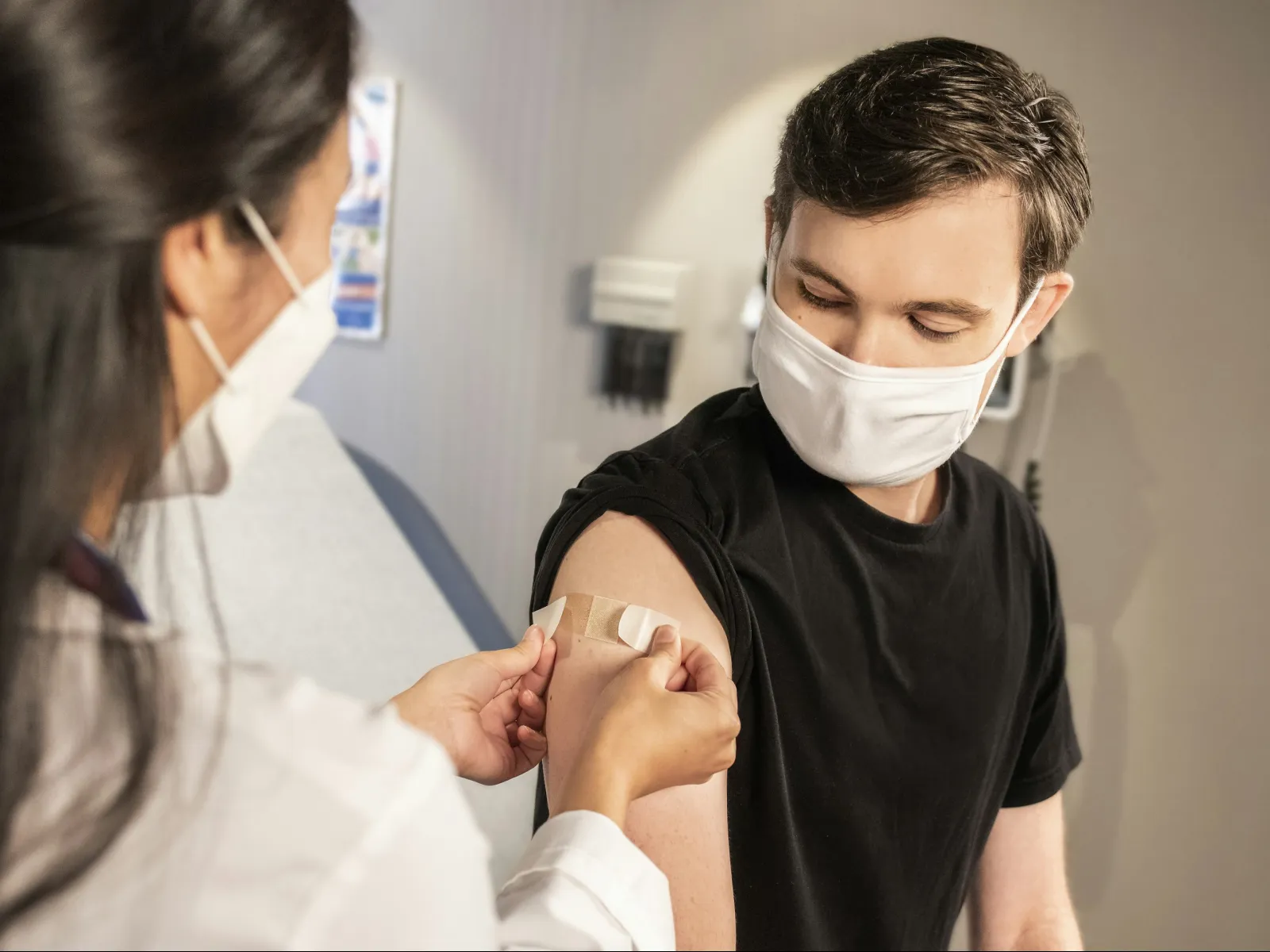Healthcare worker applies adhesive bandages on young man's arm after vaccination in clinic.