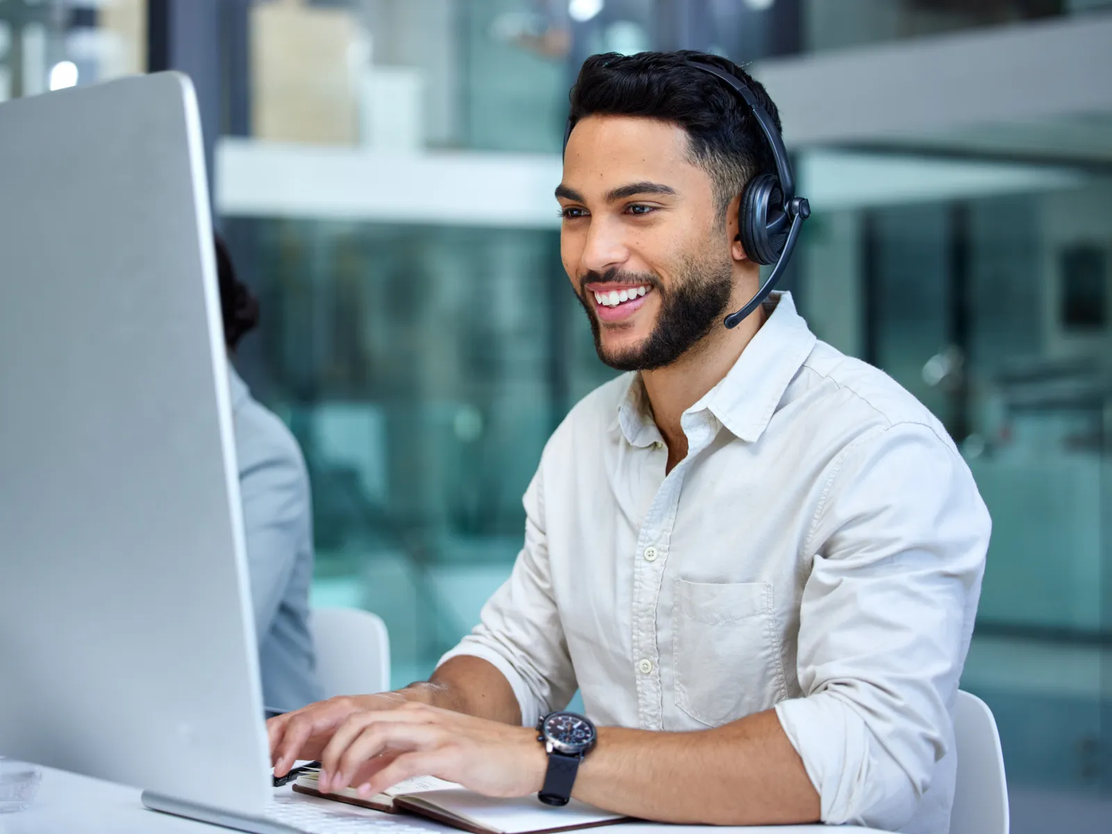 Smiling man wearing headset working on desktop computer in modern office environment