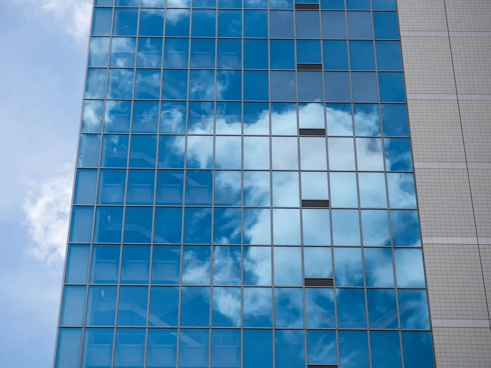 Reflective glass windows on skyscraper showing blue sky and white clouds on a sunny day.